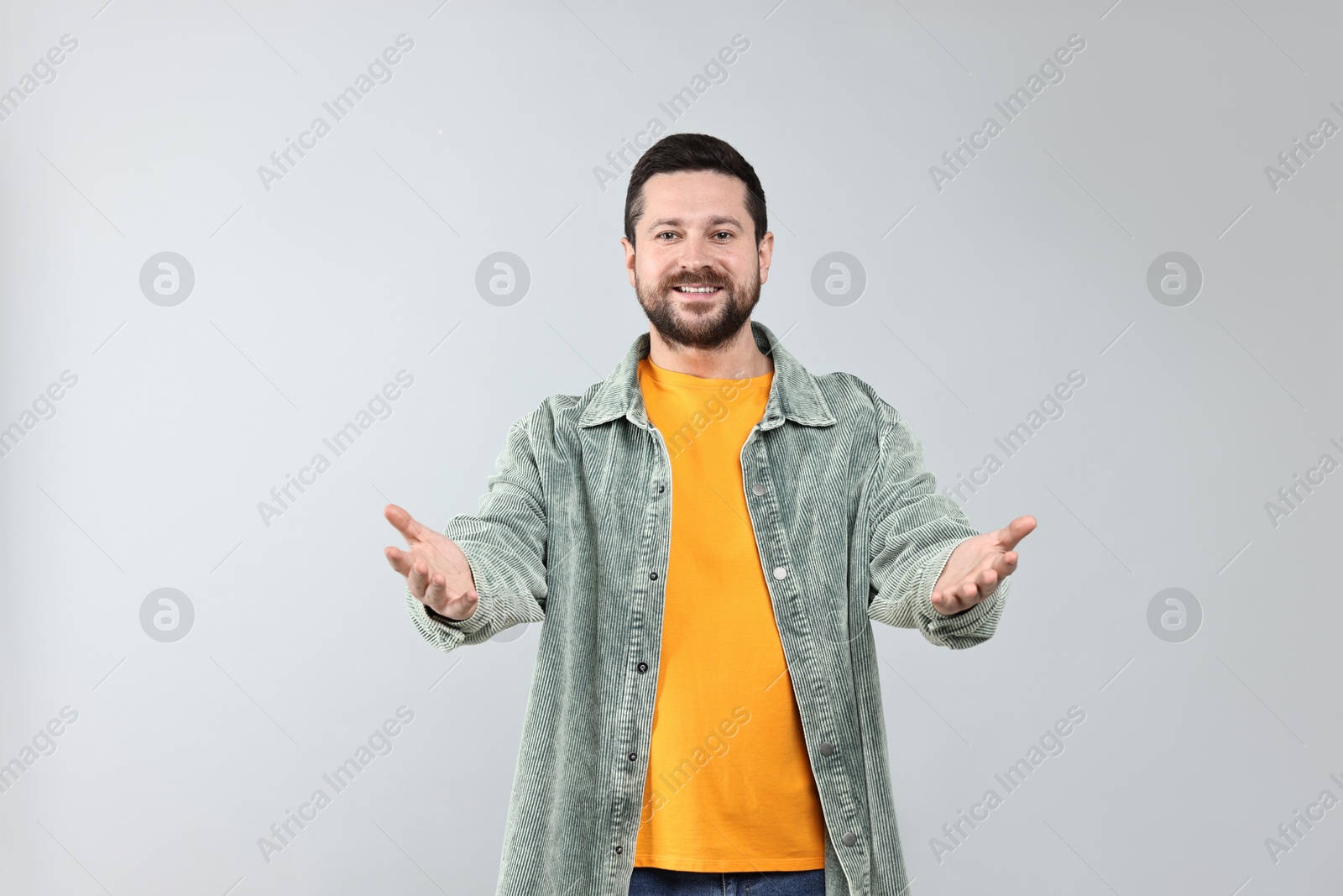 Photo of Happy man welcoming friends or guests on grey background