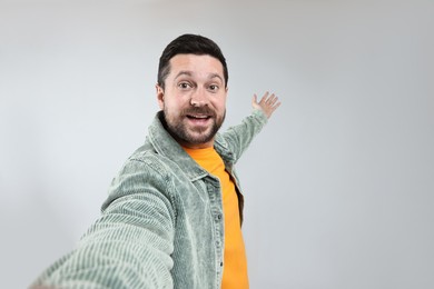 Photo of Happy man taking selfie and welcoming friends or guests on grey background