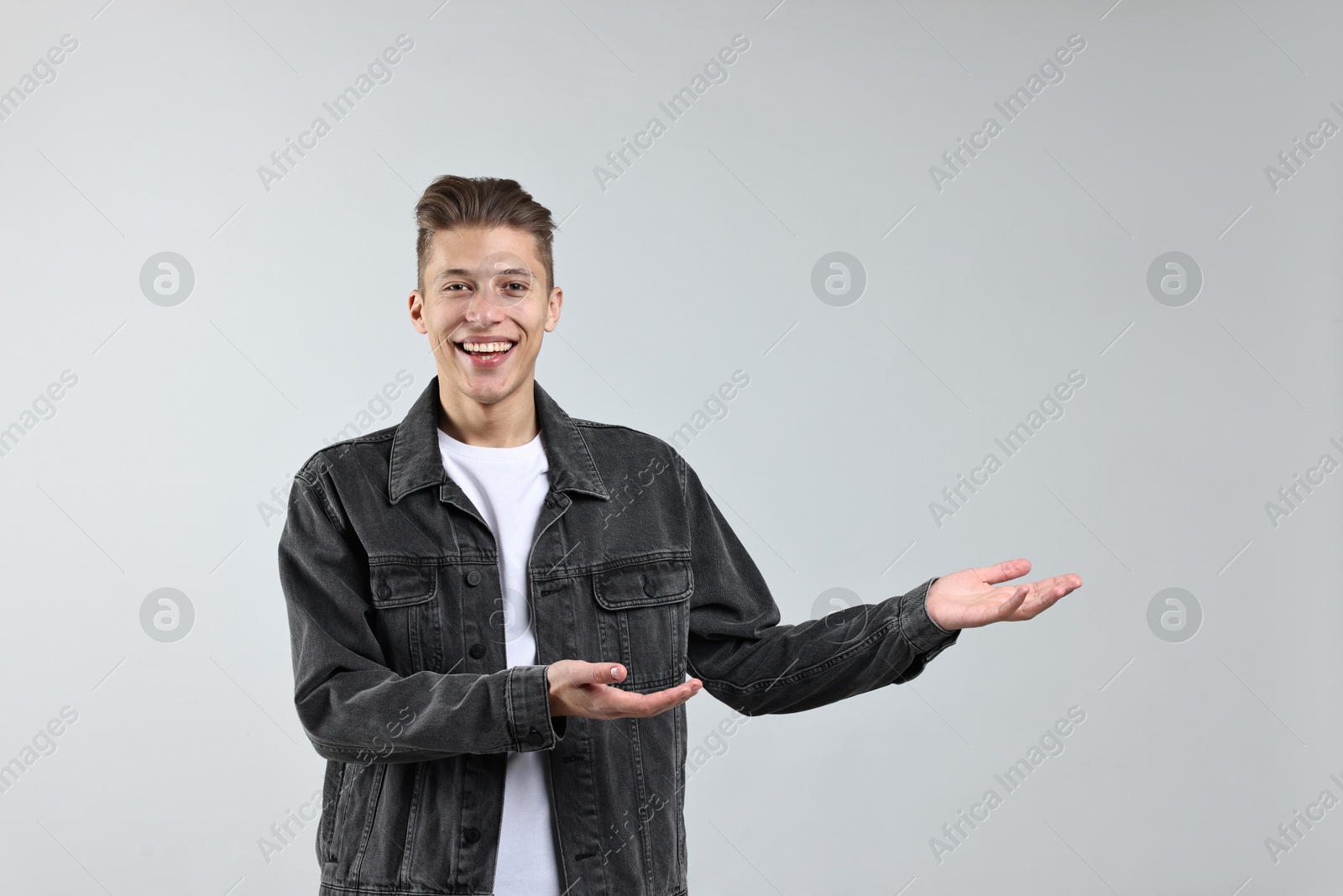 Photo of Happy man welcoming friends or guests on grey background