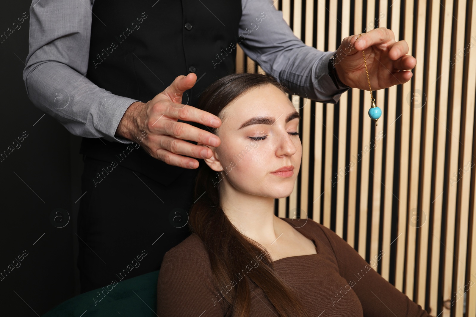 Photo of Psychologist using pendulum while working with patient during hypnosis session indoors, closeup