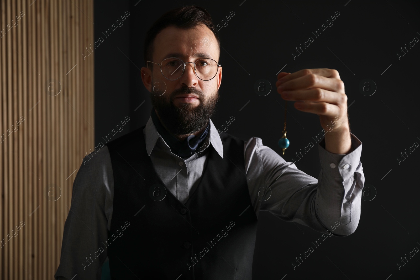 Photo of Hypnosis session. Man in glasses swinging pendulum indoors