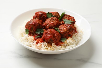 Photo of Delicious meatballs with rice, sauce and parsley on white marble table, closeup