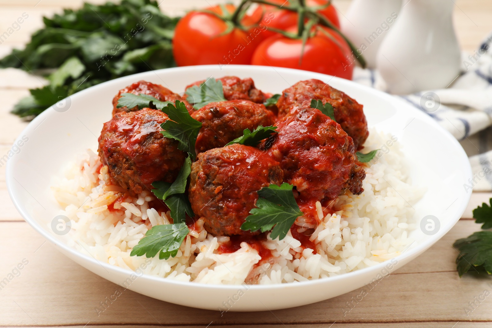 Photo of Delicious meatballs with rice, sauce and parsley on light wooden table, closeup