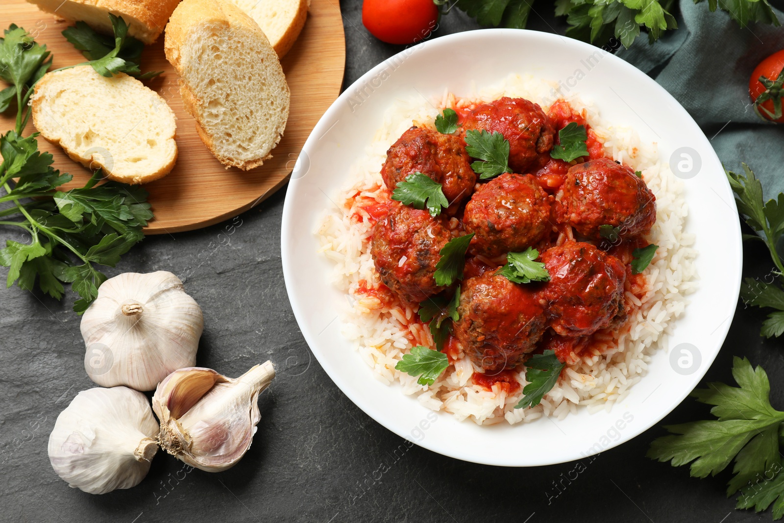 Photo of Tasty meatballs with sauce, rice and products on black table, flat lay