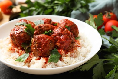 Photo of Tasty meatballs with sauce, rice and products on black table, closeup