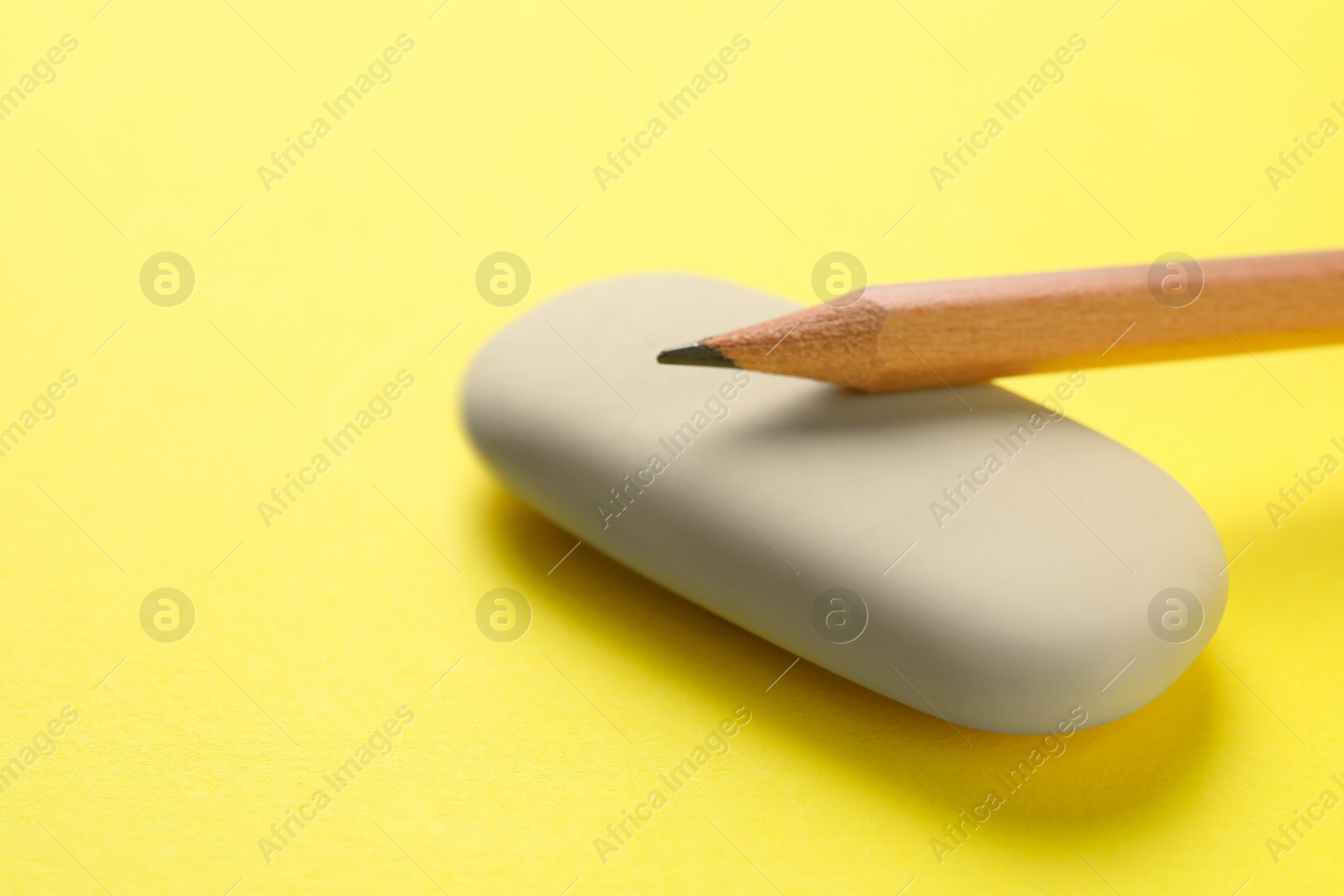 Photo of Eraser and pencil on yellow background, closeup