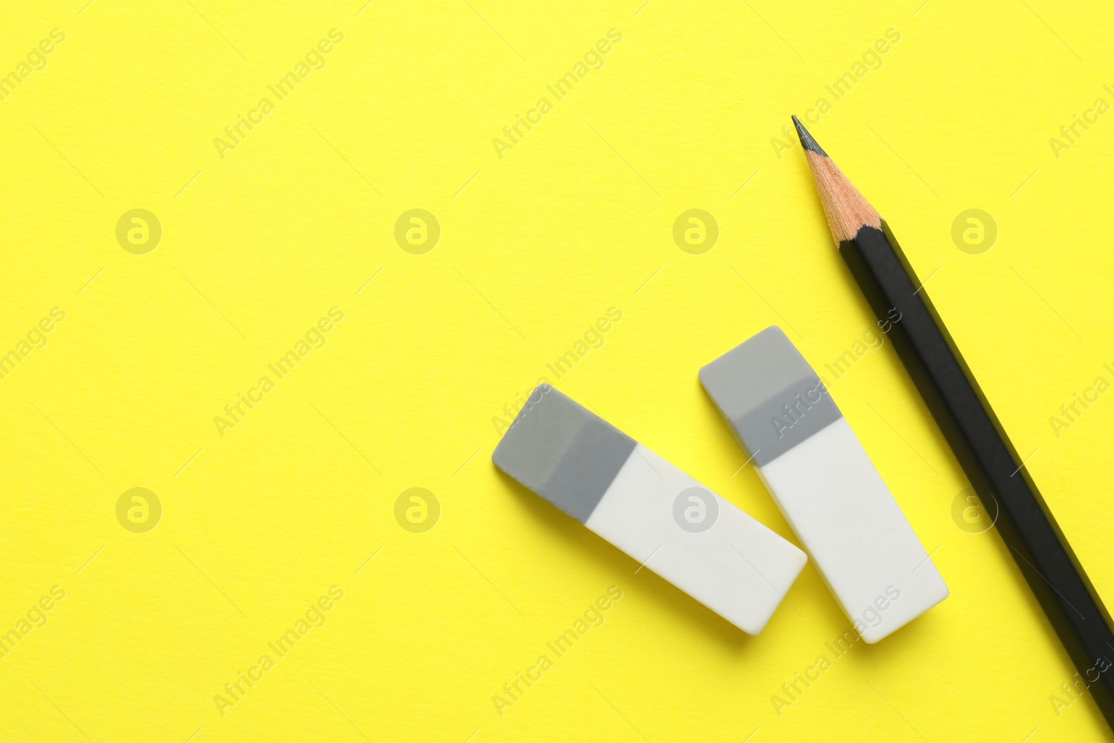 Photo of Erasers and pencil on yellow background, top view. Space for text