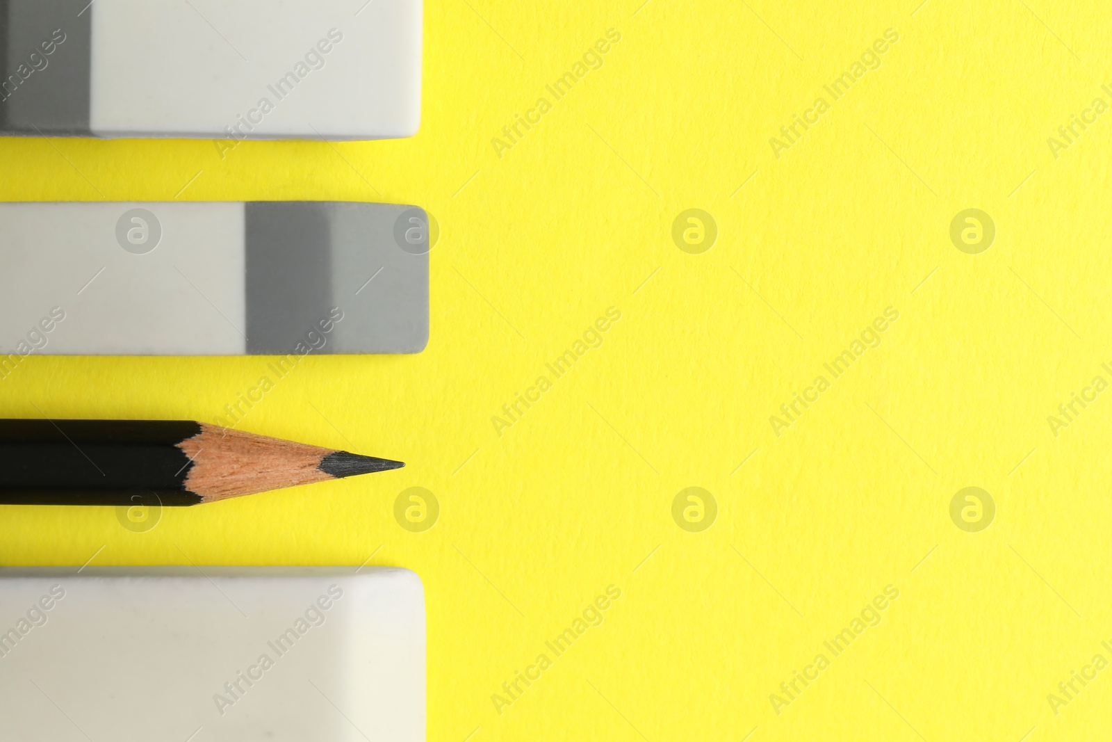 Photo of Erasers and pencil on yellow background, flat lay. Space for text