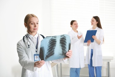 Photo of Doctor examining chest x-ray in clinic. Medical assistants with clipboard indoors