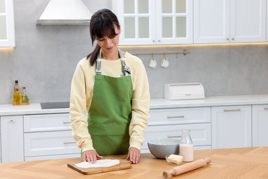 Photo of Woman sprinkling flour onto wooden board before rolling dough at table indoors. Space for text