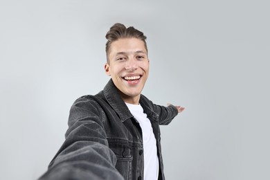 Photo of Happy man taking selfie and welcoming friends or guests on grey background