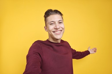 Photo of Happy man taking selfie and welcoming friends or guests on orange background