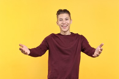 Photo of Happy man welcoming friends or guests on yellow background