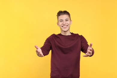 Photo of Happy man welcoming friends or guests on yellow background