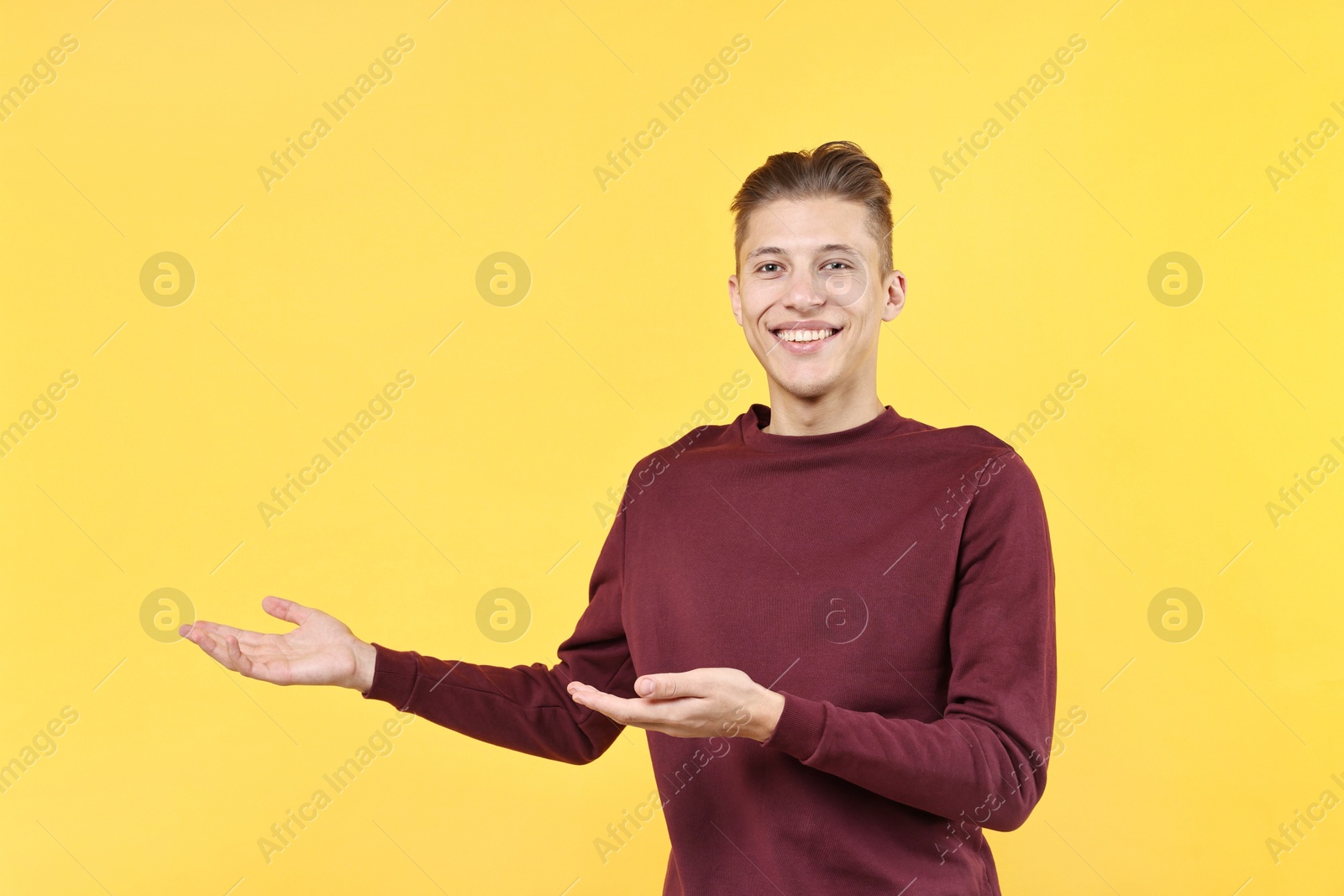 Photo of Happy man welcoming friends or guests on yellow background