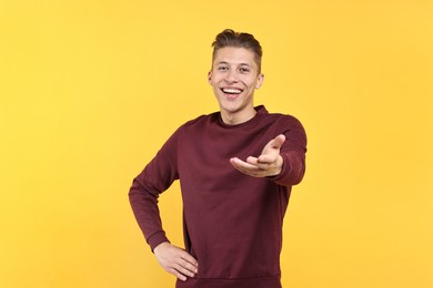 Photo of Happy man welcoming friends or guests on yellow background