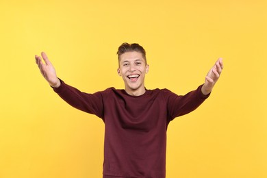 Photo of Happy man welcoming friends or guests on yellow background