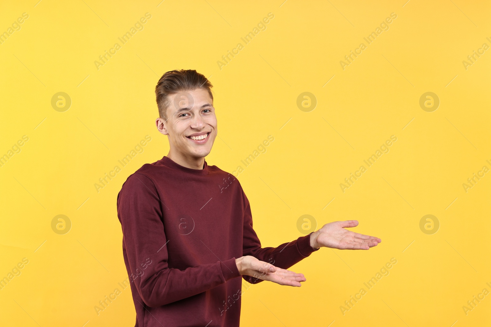 Photo of Happy man welcoming friends or guests on yellow background