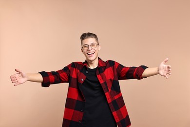 Photo of Happy man welcoming friends or guests with wide open arms on beige background