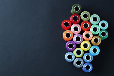 Photo of Spools of colorful sewing threads on black background, flat lay. Space for text