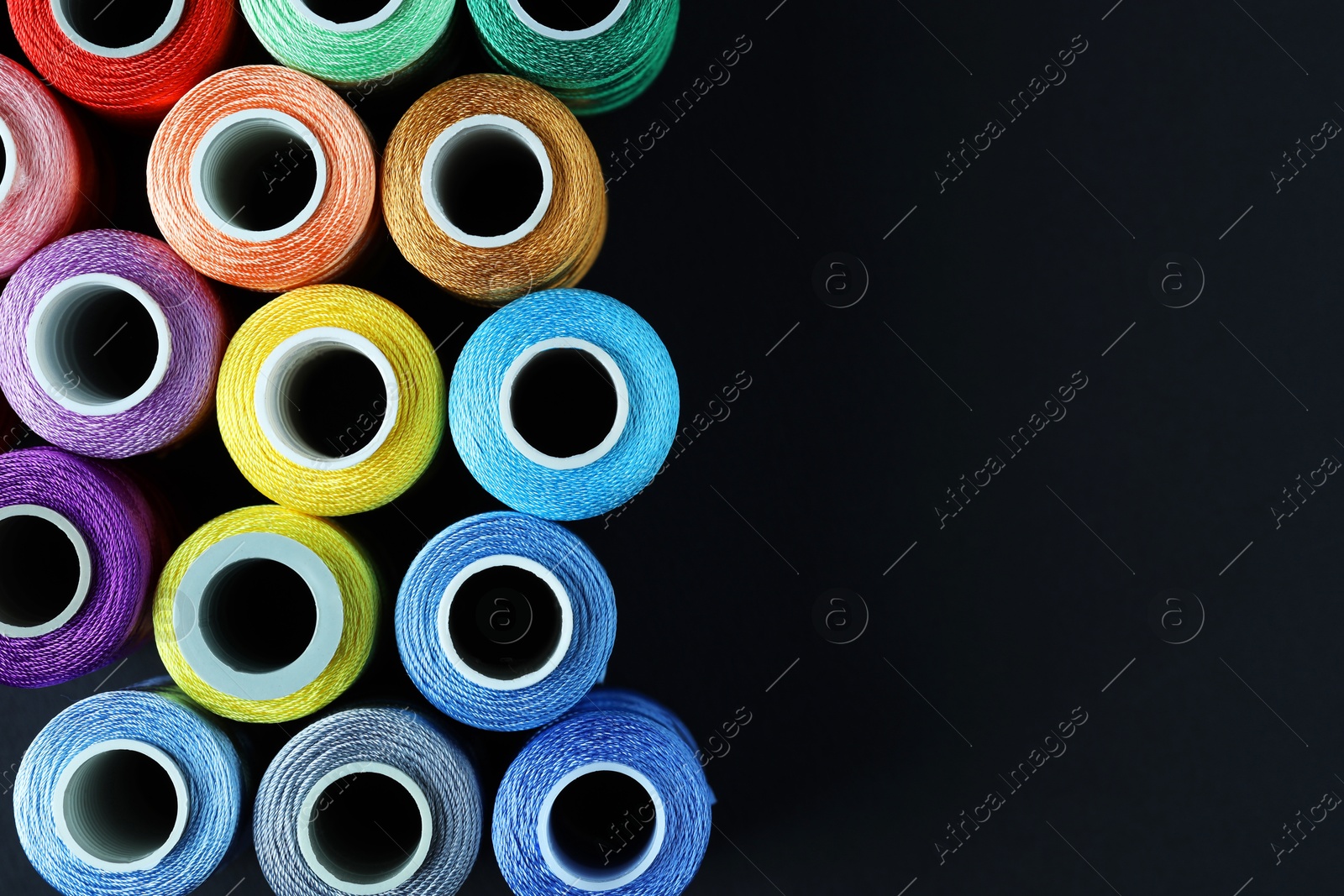 Photo of Spools of colorful sewing threads on black background, flat lay. Space for text