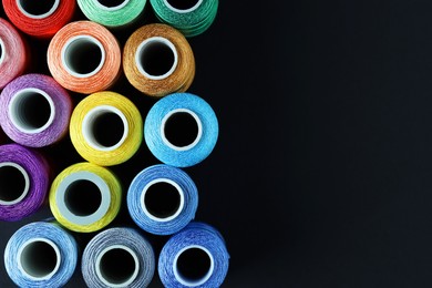 Photo of Spools of colorful sewing threads on black background, flat lay. Space for text