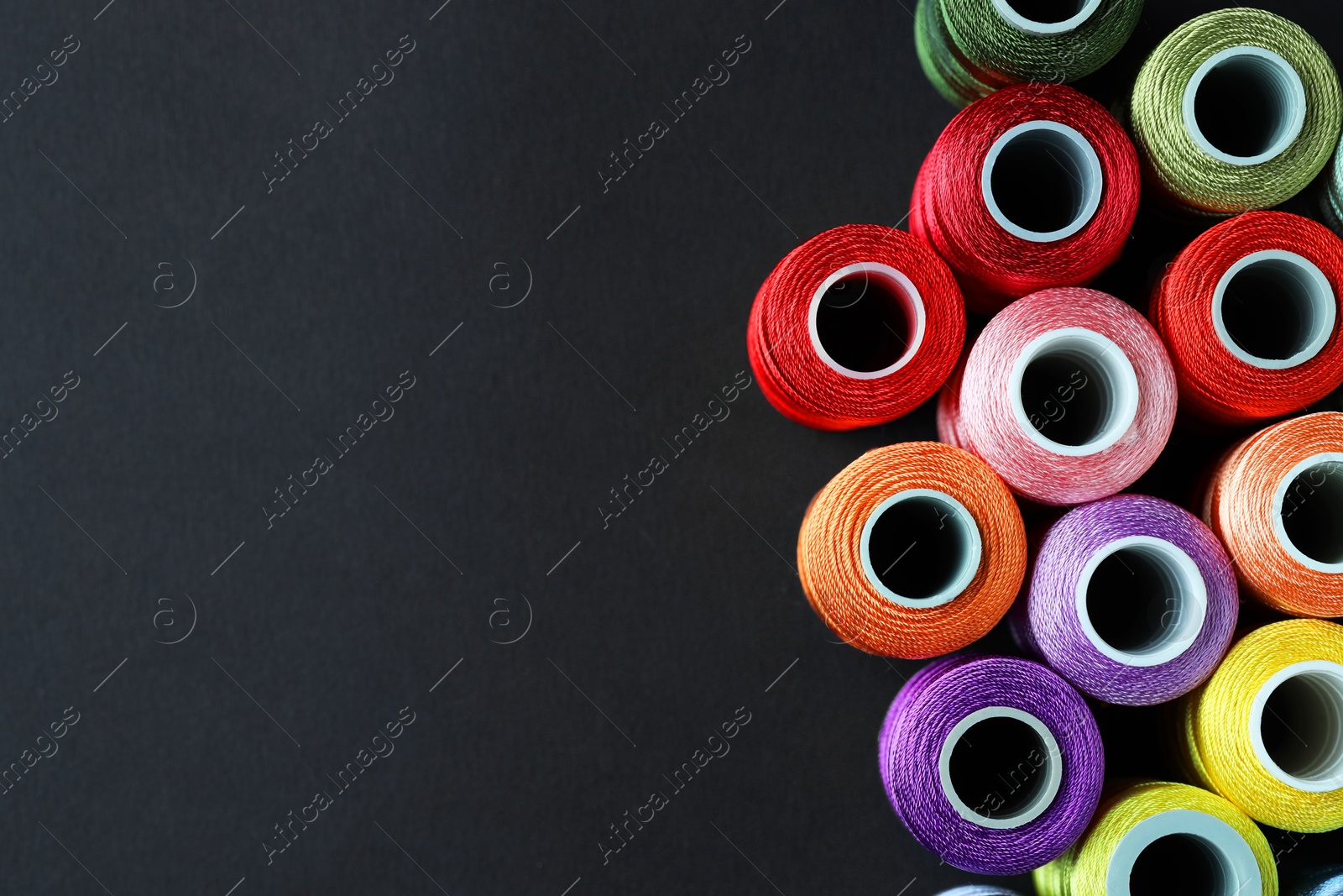 Photo of Spools of colorful sewing threads on black background, flat lay. Space for text