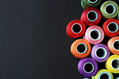 Photo of Spools of colorful sewing threads on black background, flat lay. Space for text