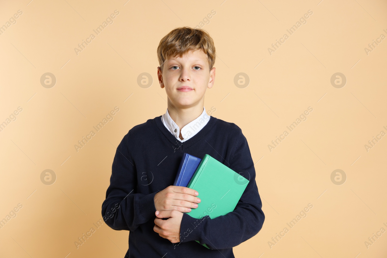 Photo of Portrait of teenage boy with books on beige background