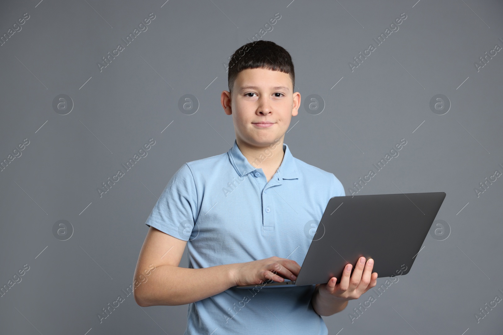 Photo of Portrait of teenage boy with laptop on grey background