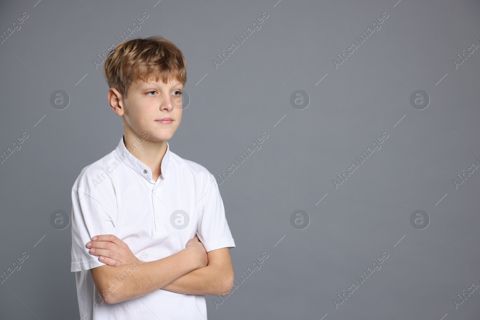 Photo of Portrait of teenage boy with crossed arms on grey background, space for text