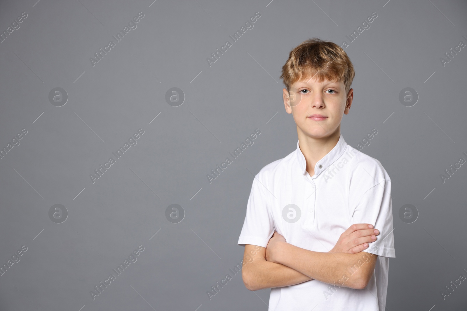 Photo of Portrait of teenage boy with crossed arms on grey background, space for text