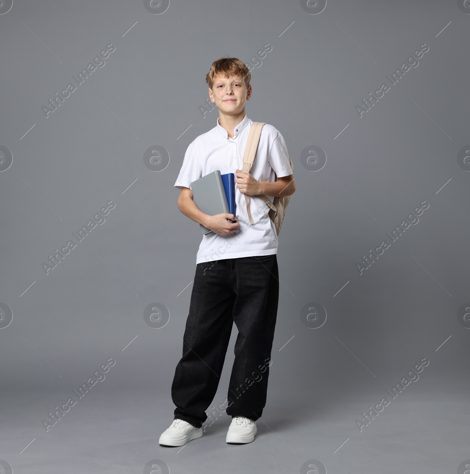 Photo of Full length portrait of teenage boy with books and backpack on grey background