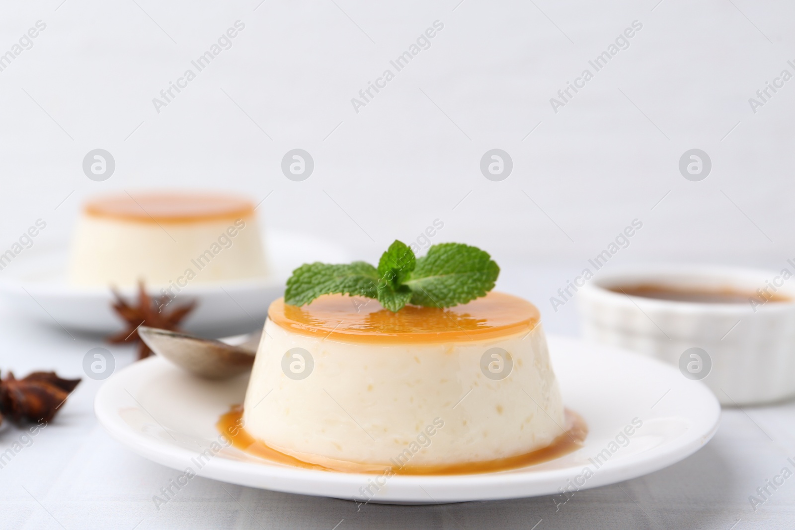 Photo of Tasty pudding with caramel sauce served on white tiled table, closeup