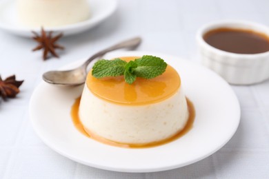 Photo of Tasty pudding with caramel sauce served on white tiled table, closeup