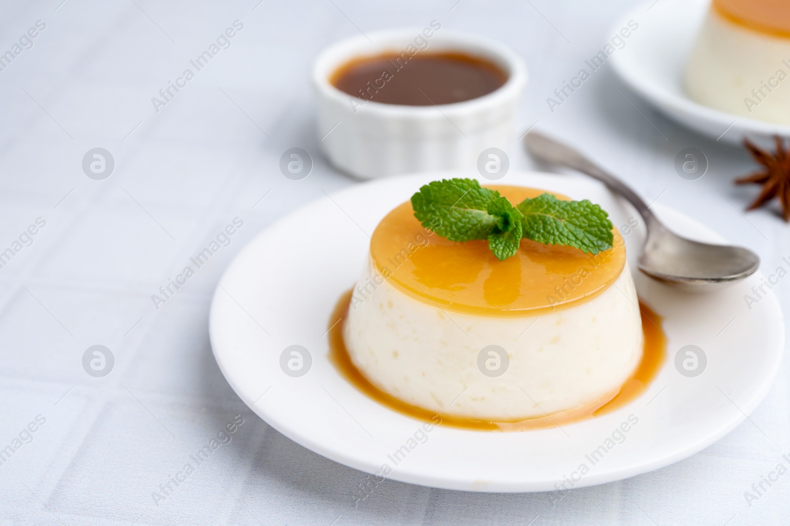 Photo of Tasty pudding with caramel sauce served on white tiled table, closeup. Space for text