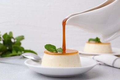 Photo of Pouring caramel sauce onto tasty pudding on white table, closeup