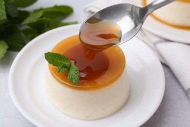 Photo of Pouring caramel sauce onto tasty pudding on white table, closeup