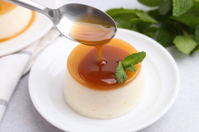 Photo of Pouring caramel sauce onto tasty pudding on white table, closeup