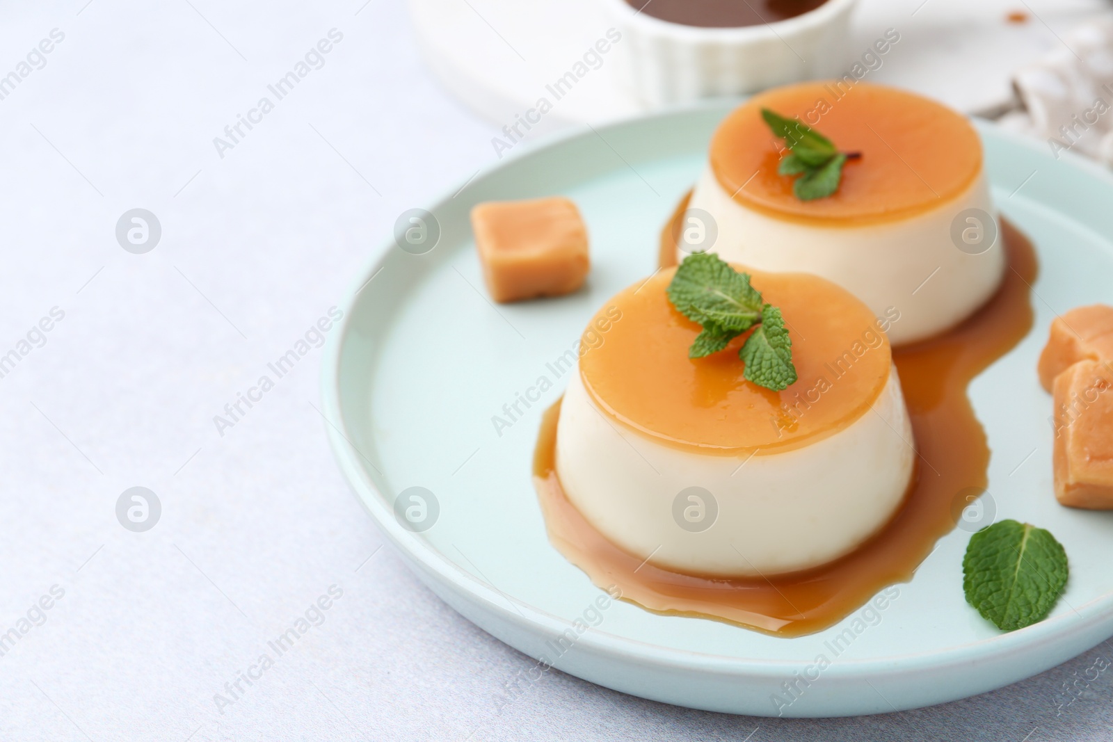 Photo of Tasty puddings with caramel sauce served on white table, closeup. Space for text