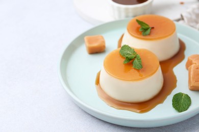 Photo of Tasty puddings with caramel sauce served on white table, closeup. Space for text