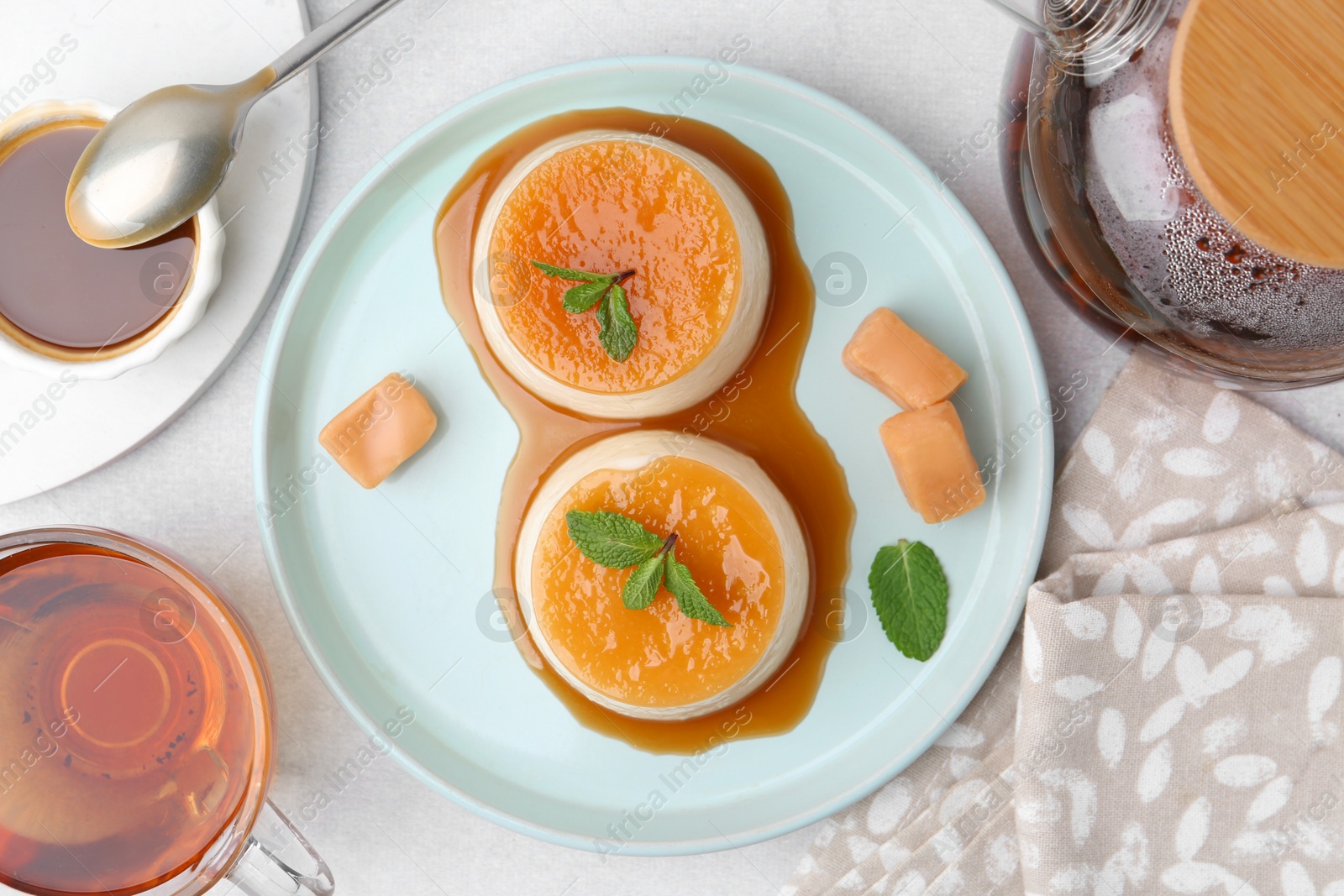 Photo of Tasty puddings with caramel sauce served on white table, flat lay