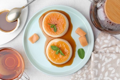 Photo of Tasty puddings with caramel sauce served on white table, flat lay