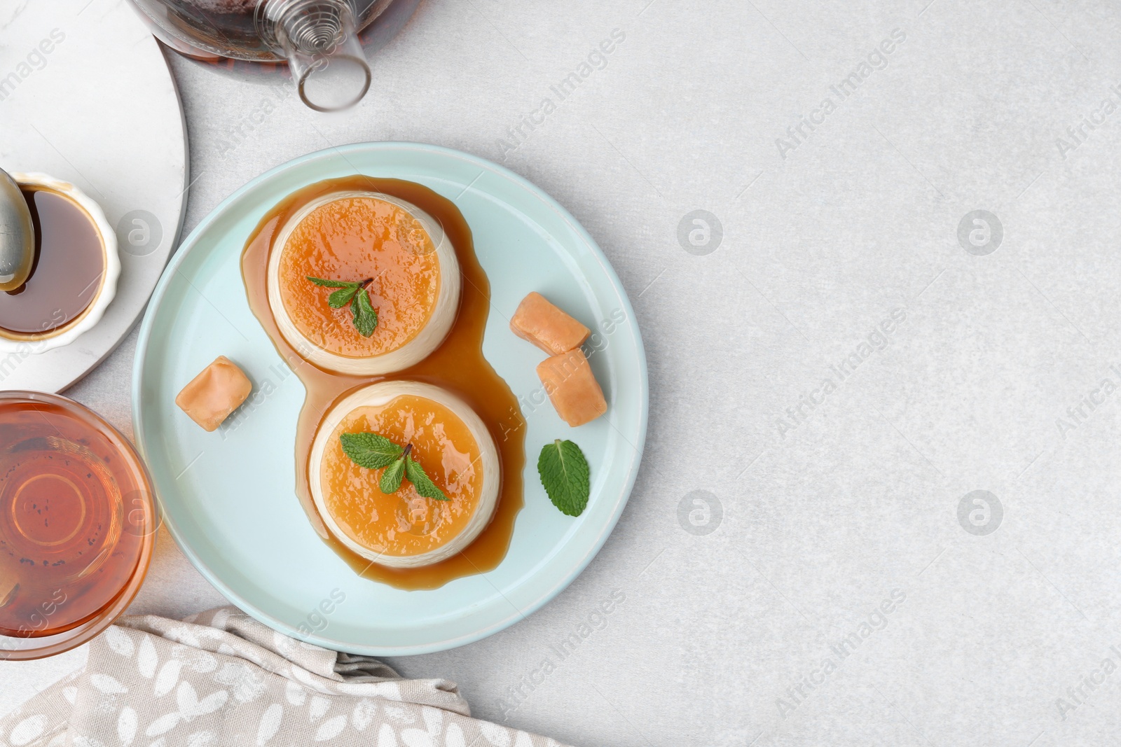 Photo of Tasty puddings with caramel sauce served on white table, flat lay. Space for text