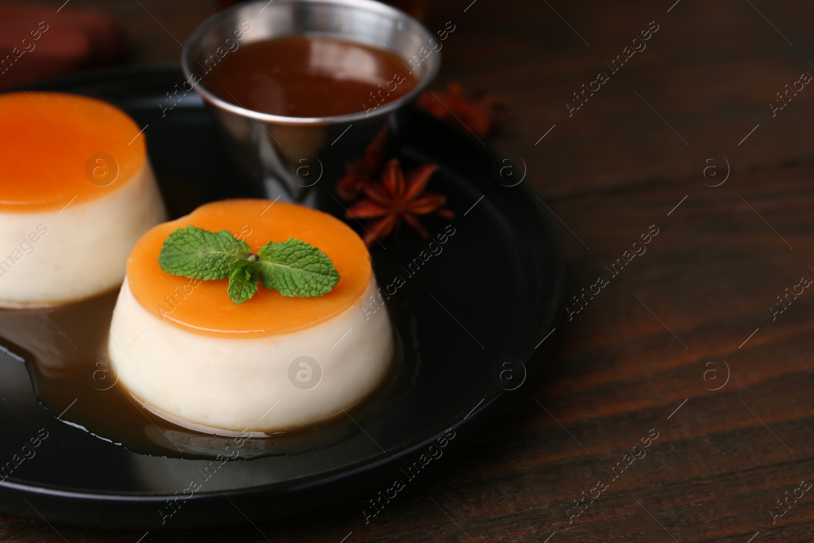 Photo of Tasty puddings with caramel sauce served on wooden table, closeup. Space for text