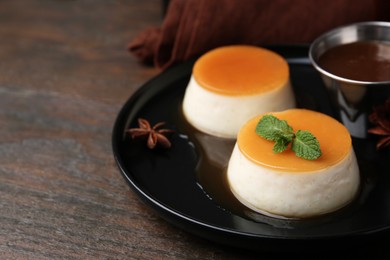 Photo of Tasty puddings with caramel sauce served on wooden table, closeup. Space for text