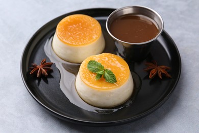 Photo of Tasty puddings with caramel sauce served on light grey table, closeup