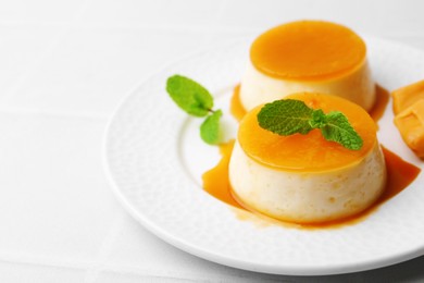 Photo of Tasty puddings with caramel sauce served on white tiled table, closeup. Space for text