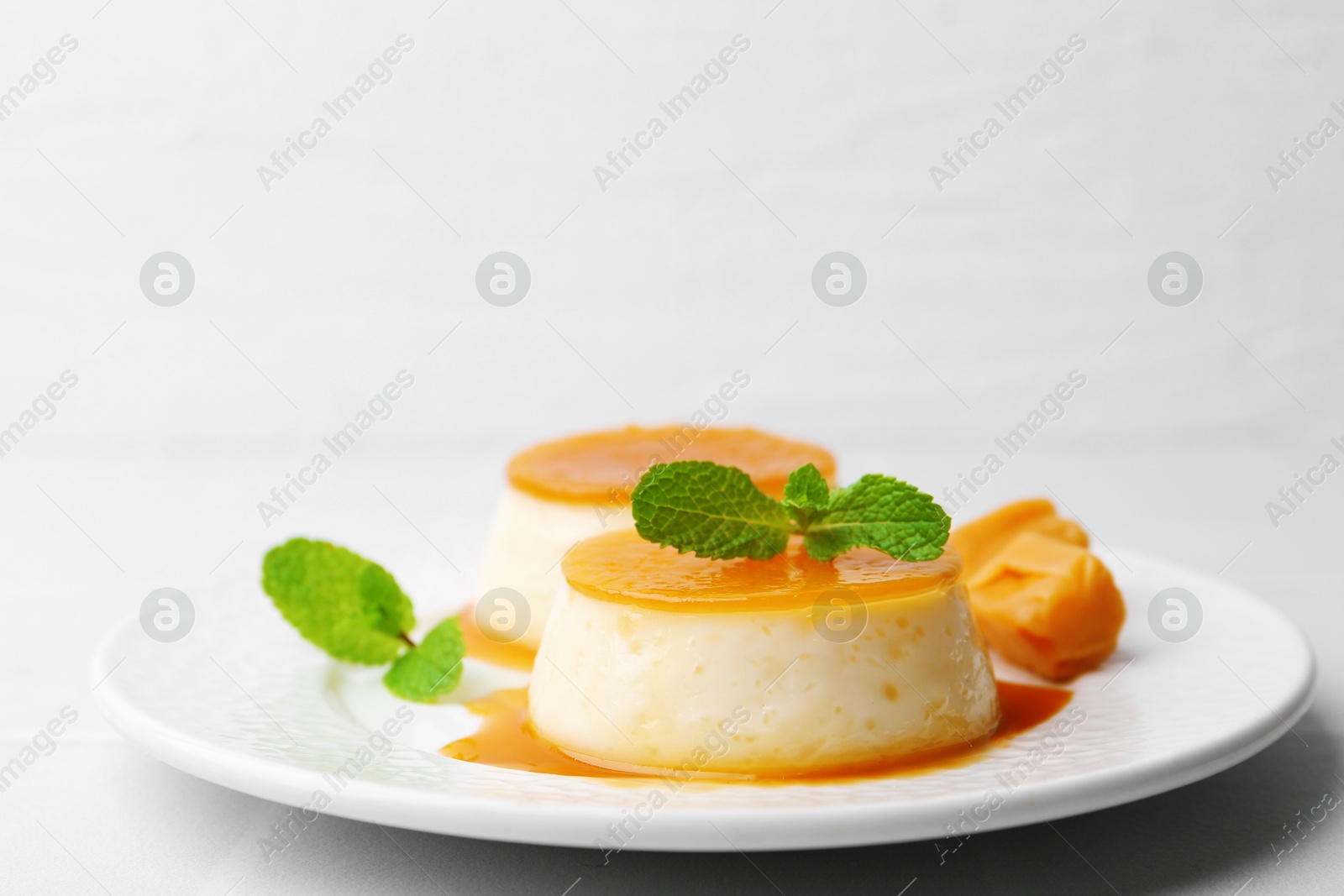 Photo of Tasty puddings with caramel sauce served on white tiled table, closeup. Space for text