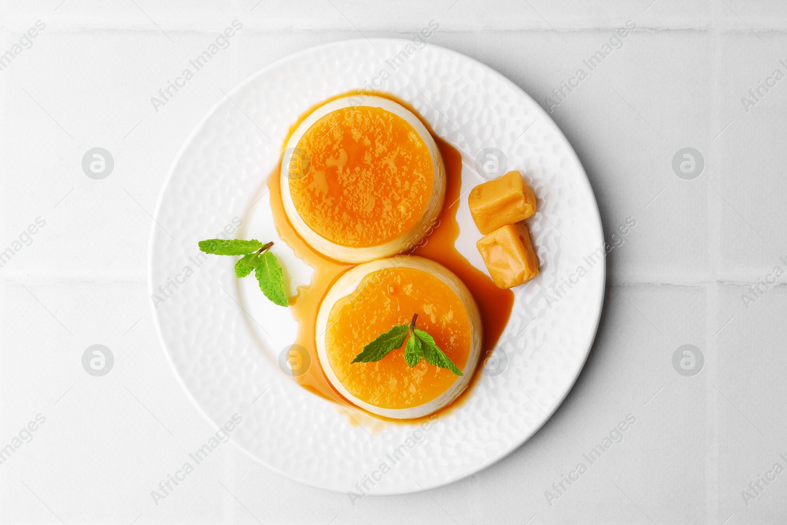 Photo of Tasty puddings with caramel sauce served on white tiled table, top view